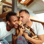 Couple in matching pajamas smile and hold small dog.